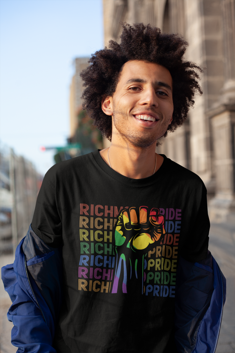 A handsome man looking at the camera and smiling, while wearing a Richmond Pride t-shirt.