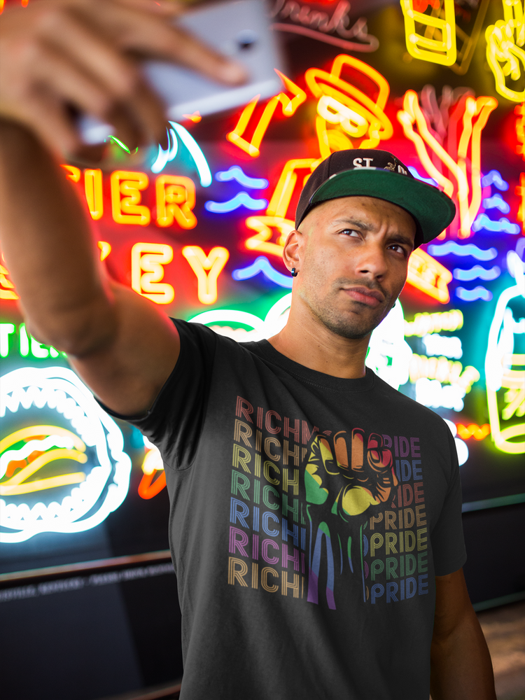 A man taking a selfie in from of a wall of neon signs, while wearing a Richmond Pride t-shirt.