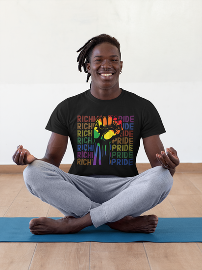 A guy with a nose ring sitting on a yoga mat, in a yoya pose, smiling at the camera while wearing a Richmond Pride t-shirt.