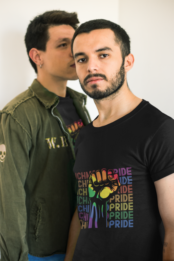 A man whispering into another man while both wearing black shirts with the words Richmond Pride in different colors per row being a rainbow fist.