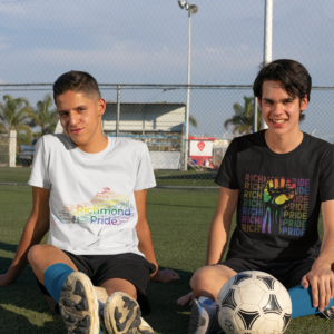 Two teenagers wearing Richmond Pride shirts. One shirt is white with the rainbow flag colors on the state of Kentucky and the other is wearing a the black Richmond Pride shirt with the words Richmond Pride in different colors per row behind a rainbow fist.