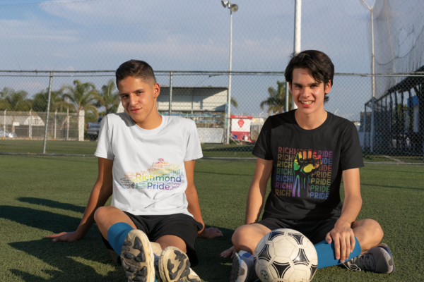 Two teenagers wearing Richmond Pride shirts. One shirt is white with the rainbow flag colors on the state of Kentucky and the other is wearing a the black Richmond Pride shirt with the words Richmond Pride in different colors per row behind a rainbow fist.